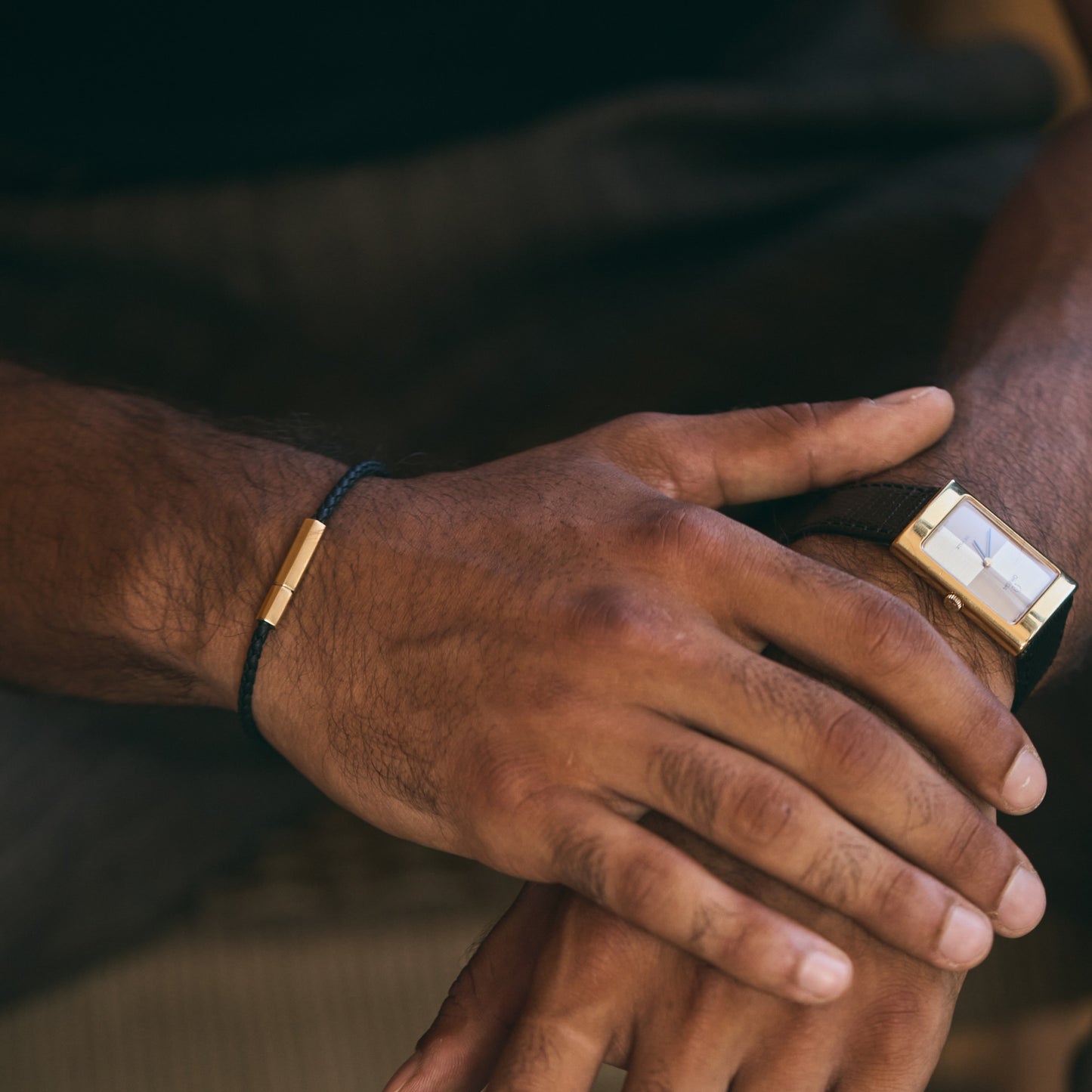 hexagonal black nappa leather bracelet with 18k yellow gold clasp worn on wrist next to rectangular watch