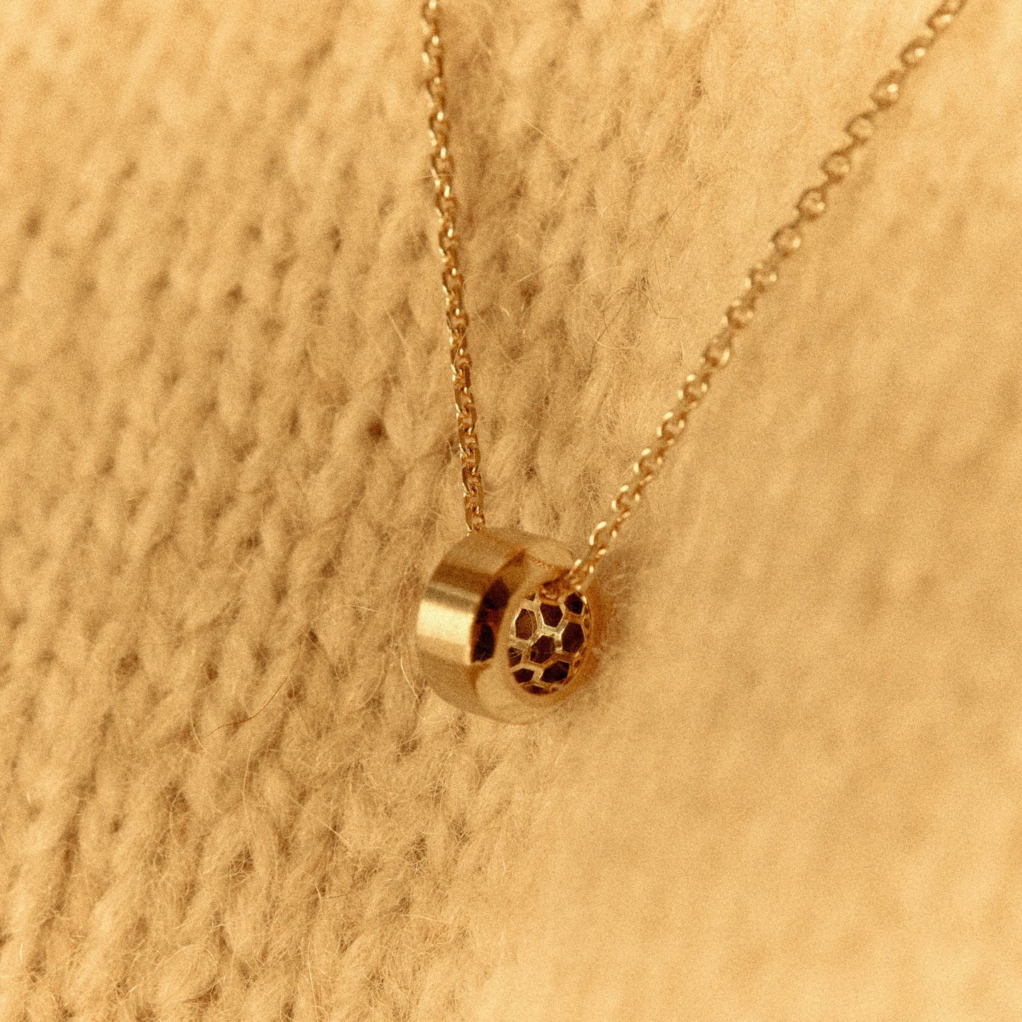 Close-up of a 18k yellow gold pendant necklace on a textured knit sweater