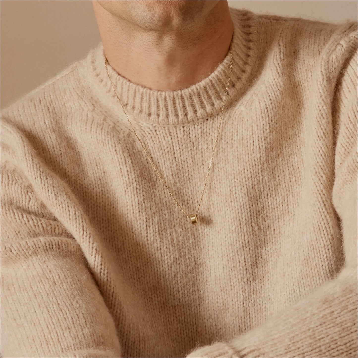 Person wearing a small gold beveled ring pendant necklace in 18k yellow gold with a cream knit sweater