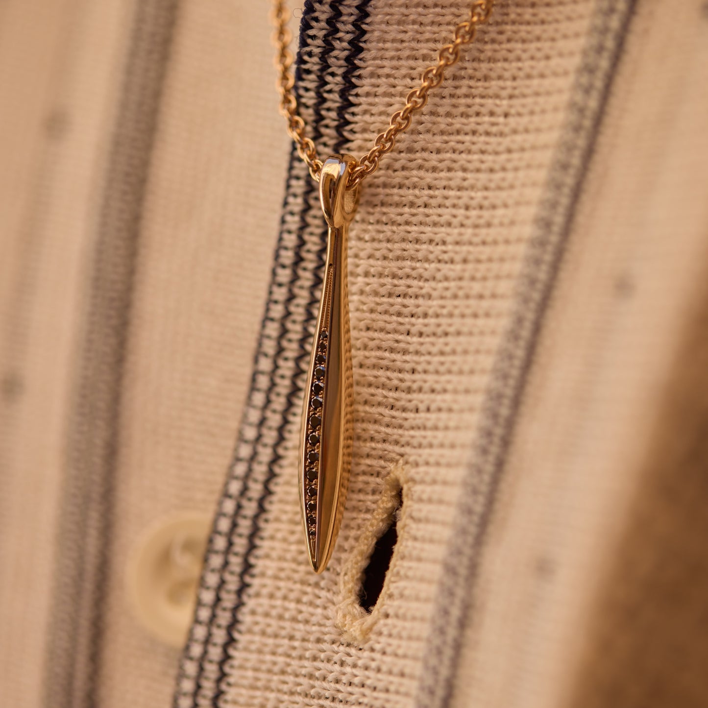 Close-up of an 18k rose gold sword pendant with black diamonds on a chain