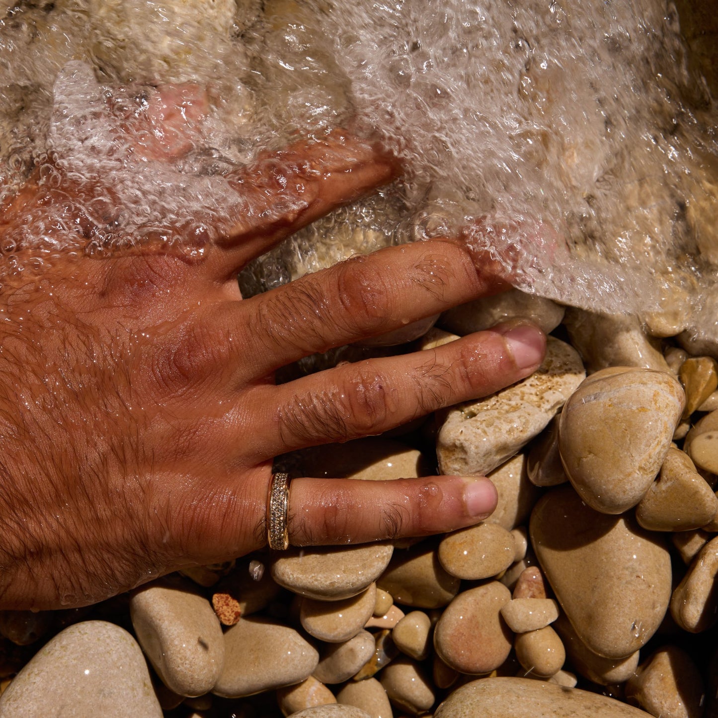 18k gold pavé band ring on wet hand in flowing water over river stones