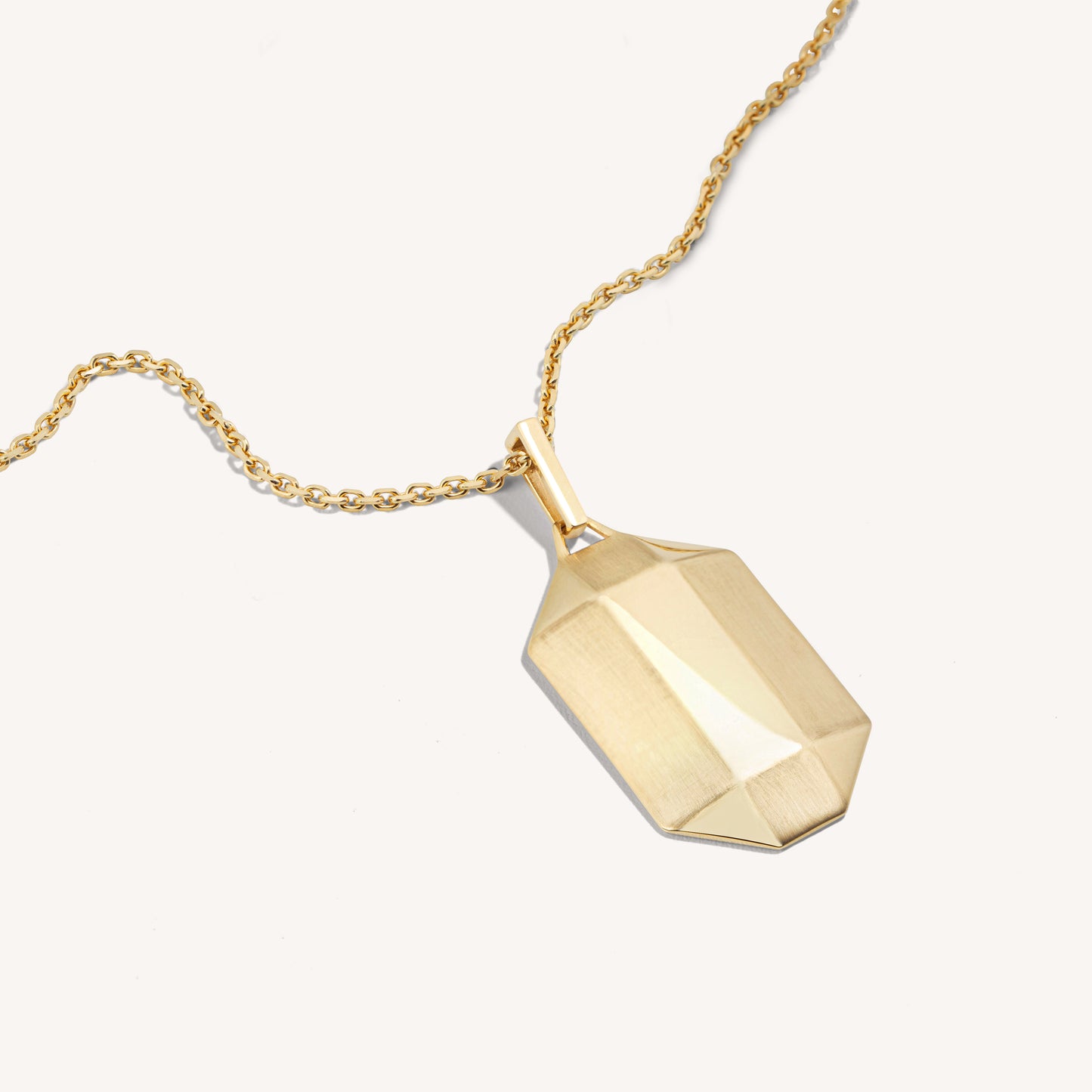 A 18k yellow gold dog tag pendant with a diamond-inspired silhouette, featuring matte and polished finishes, hanging on a gold chain.