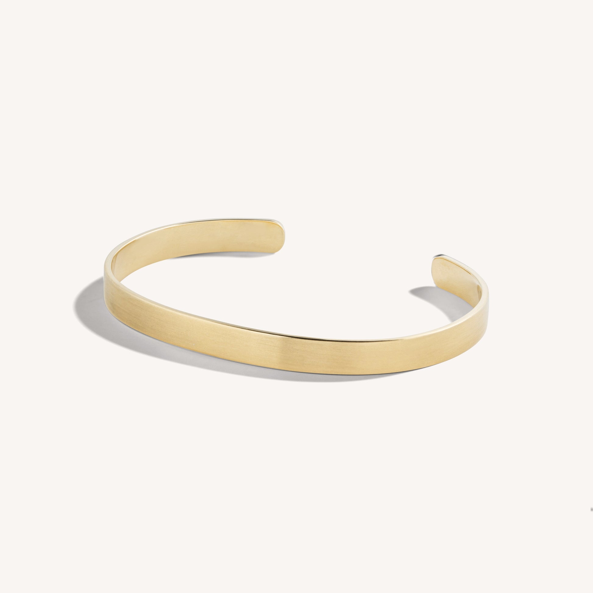 Men’s brushed 18k yellow gold open cuff bracelet with rounded edges, on white background.