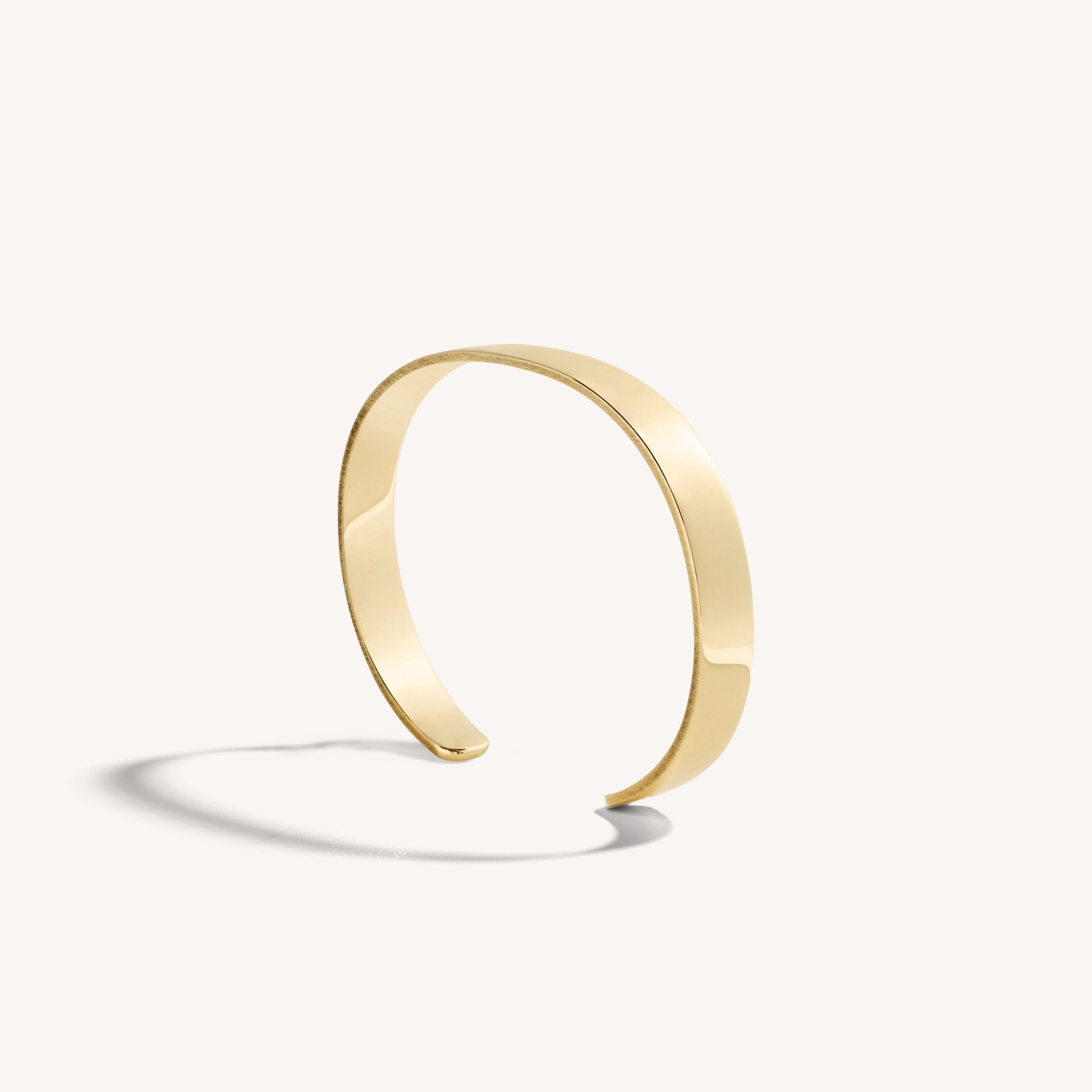 Men’s polished 18k yellow gold open cuff bracelet with rounded edges, on white background.
