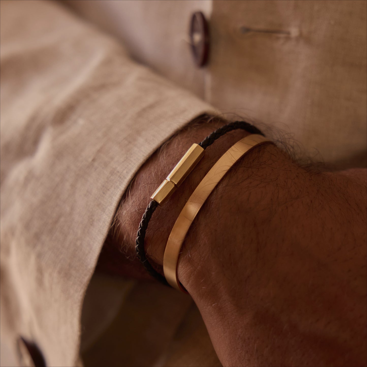 Man wearing a polished 18k rose gold cuff bracelet and a black leather bracelet with an 18k yellow gold clasp, on wrist.