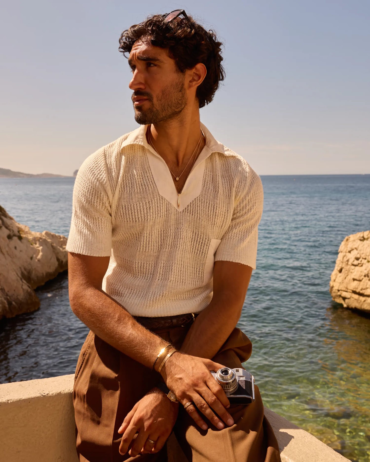 Prévaut lookbook: model seated by the sea wearing 18k recycled rose-gold cuff, leather bracelet, gold ring with black diamonds, and rose-gold pendant necklace
