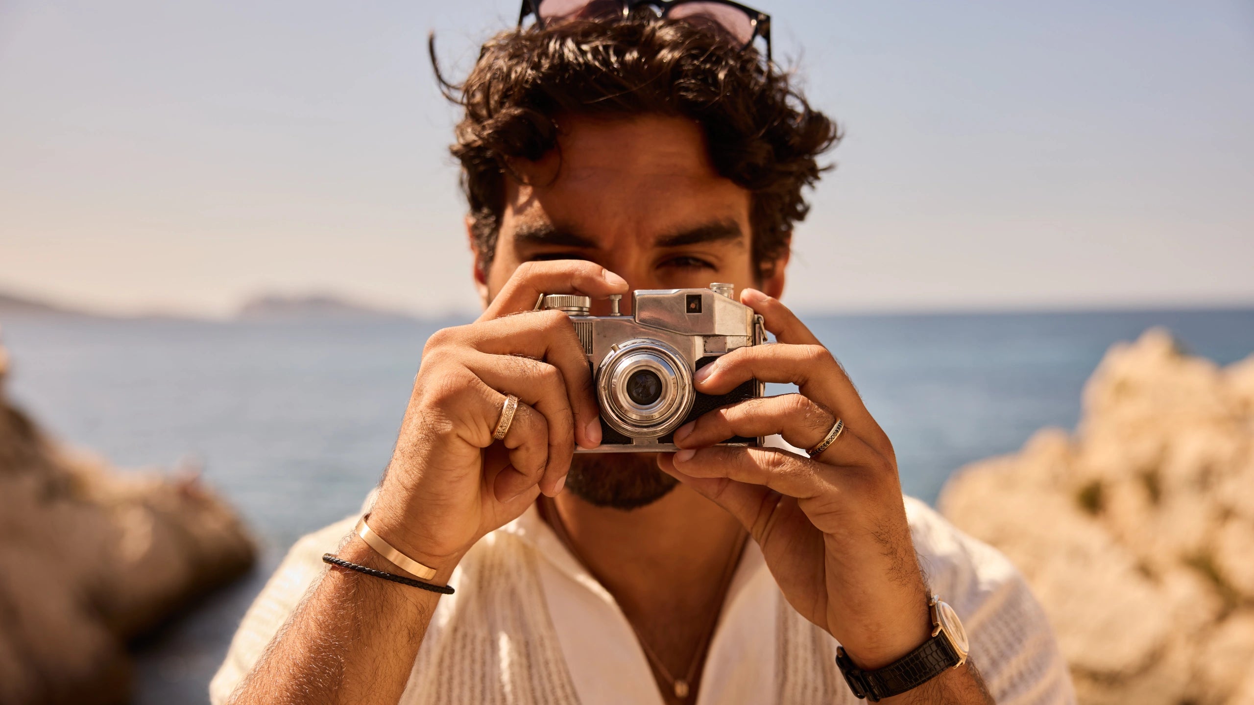 Prevaut men’s jewelry: model with vintage camera wearing 18k recycled rose-gold cuff, leather bracelet, gold rings with diamonds, and rose-gold pendant necklace