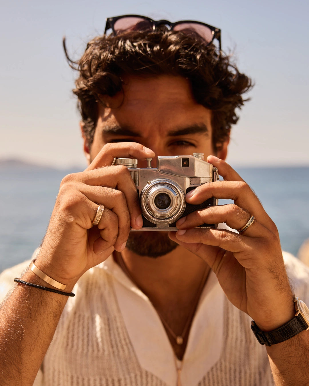Prevaut men’s jewelry: model with vintage camera wearing 18k recycled rose-gold cuff, leather bracelet, gold rings with diamonds, and rose-gold pendant necklace