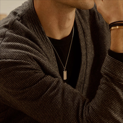 18k white gold Dog tag pendant necklace worn with a dark top and checked jacket