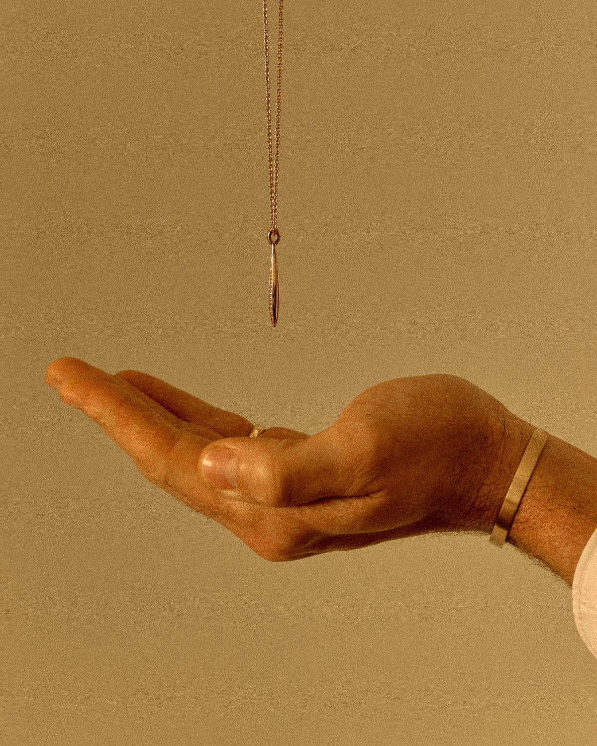 18k yellow gold pendant necklace suspended above an open hand in warm light wearing a 18k solid gold cuff