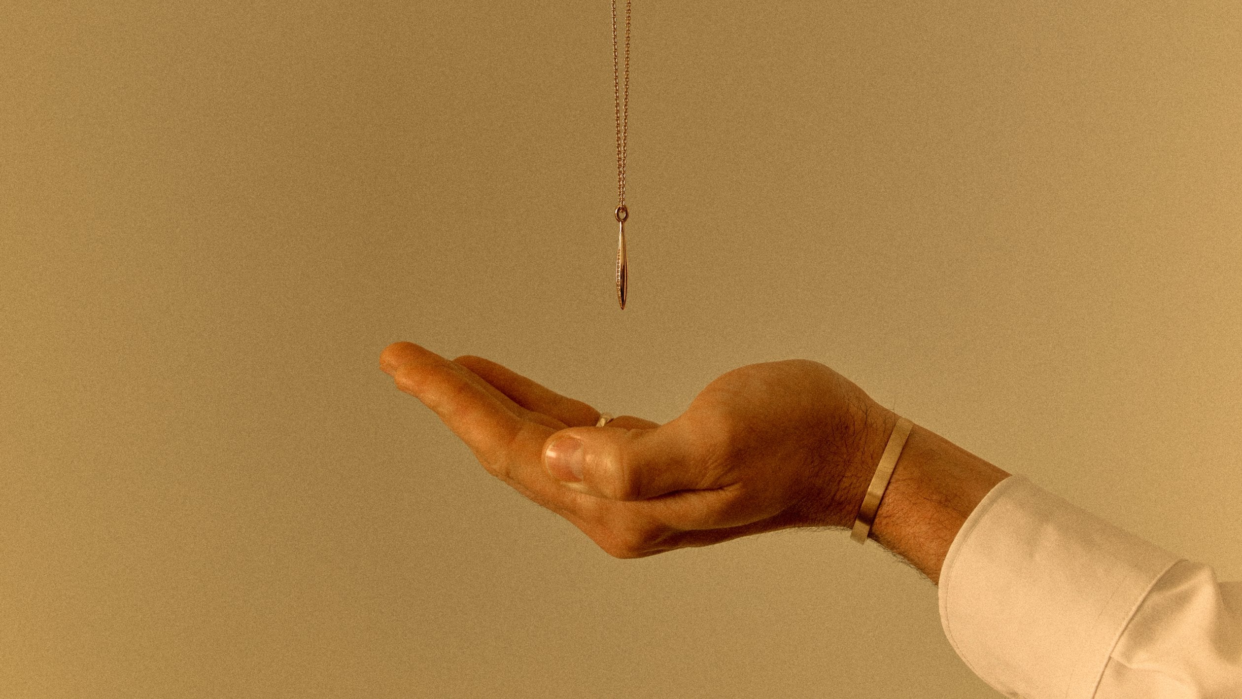 18k yellow gold pendant necklace suspended above an open hand in warm light wearing a 18k solid gold cuff