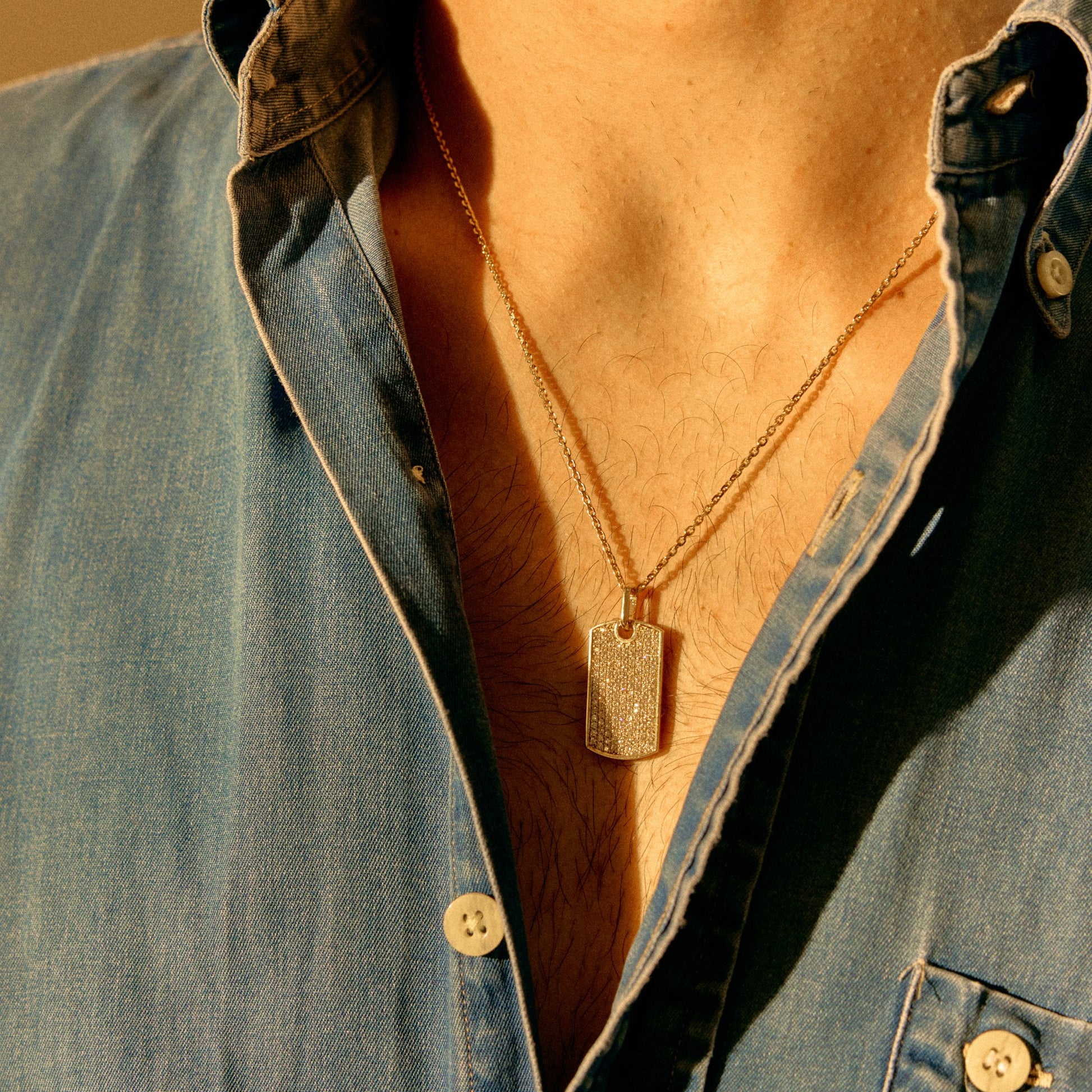 Pavé-set rectangular white diamond and 18k yellow gold pavé pendant necklace worn with an open denim shirt
