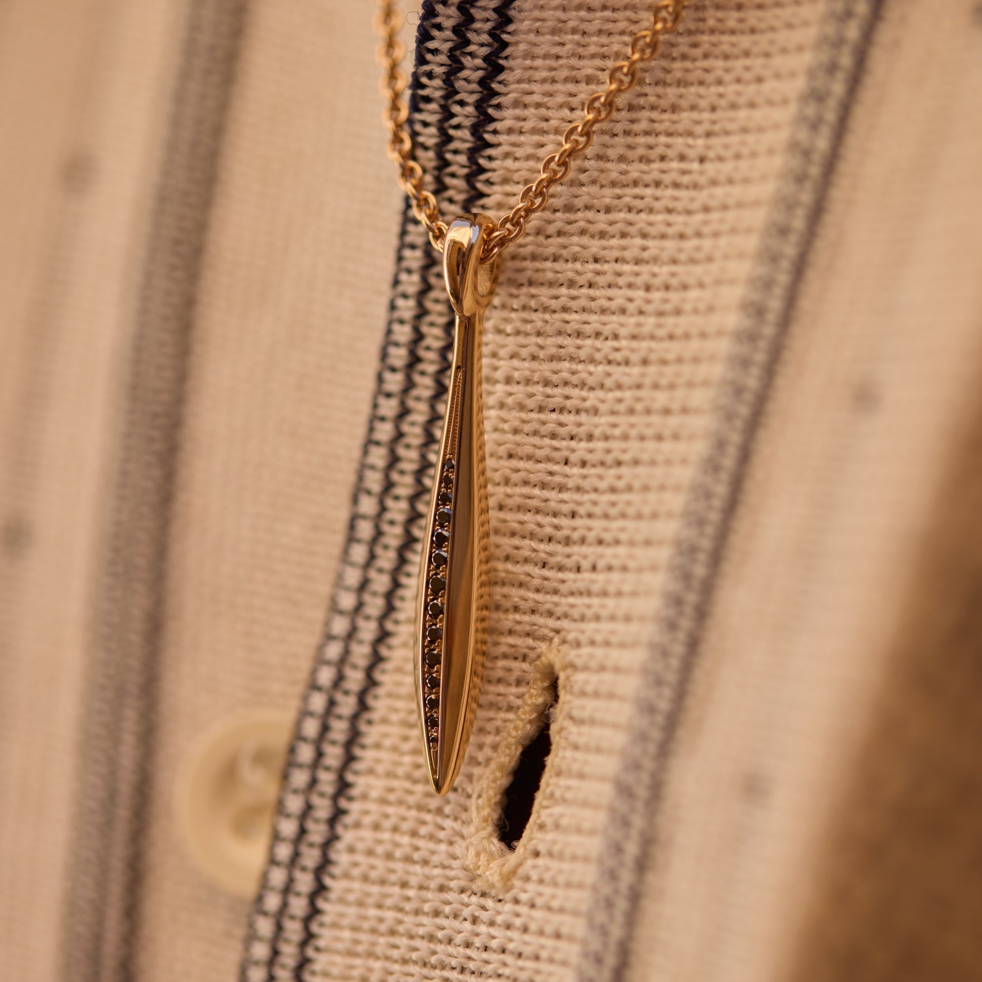 Close-up of an 18k rose gold sword pendant with black diamonds on a chain
