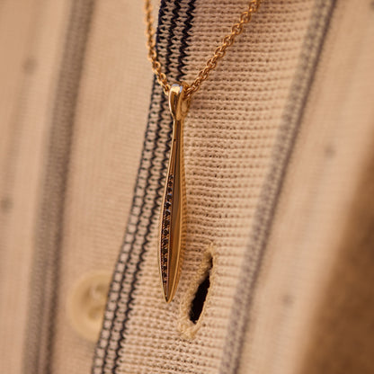 Close-up of an 18k rose gold sword pendant with black diamonds on a chain