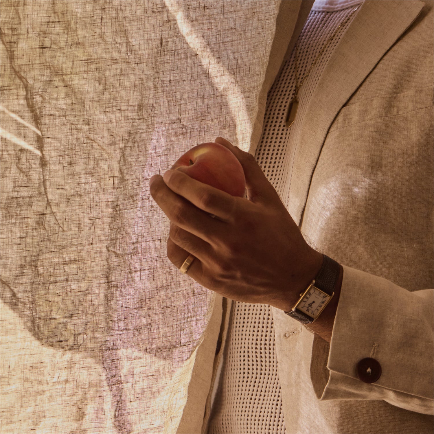 men's hand wearing 18k recycled gold ring and holding a peach.