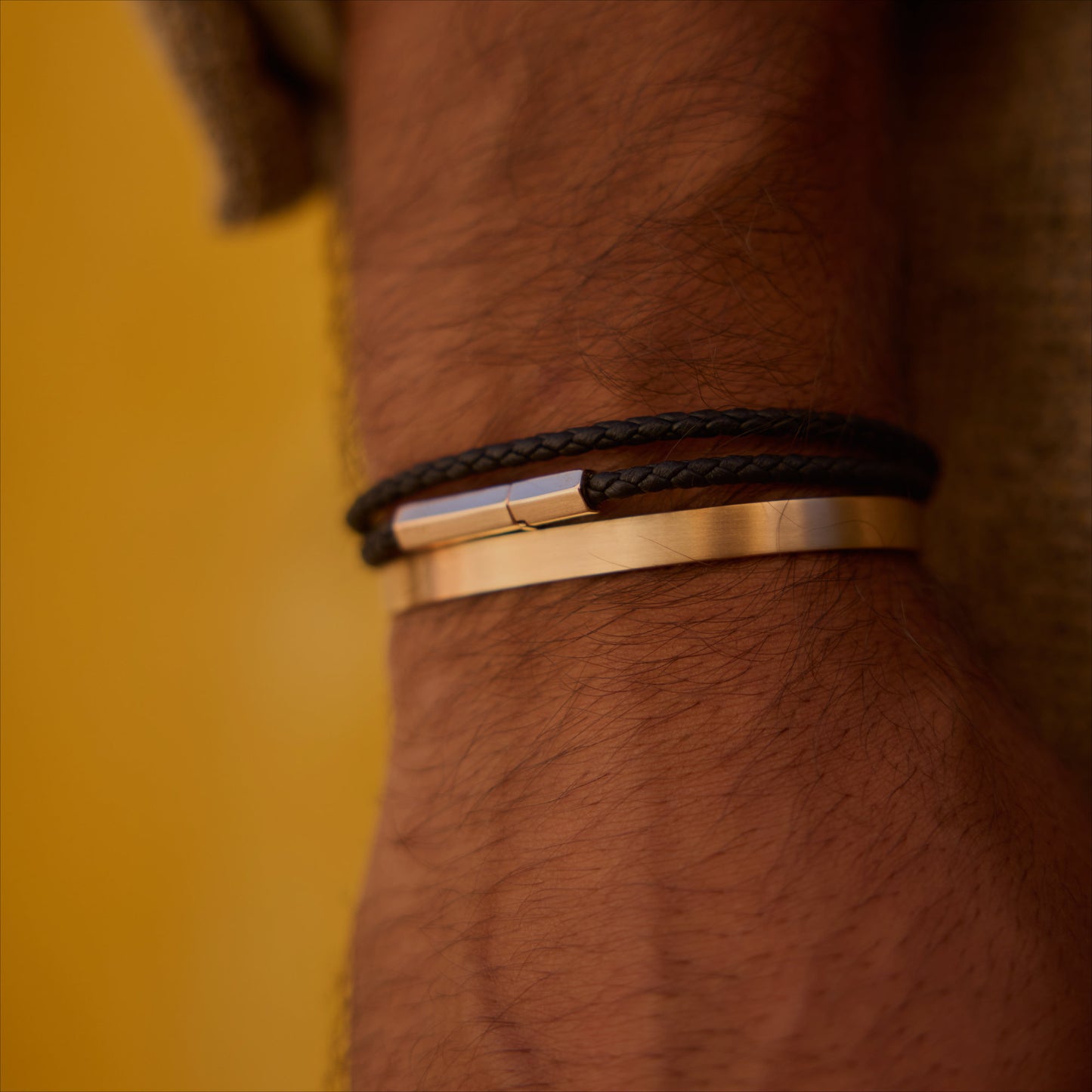 Black double-wrap hexagonal leather bracelet with 18k rose-gold clasp on wrist.
