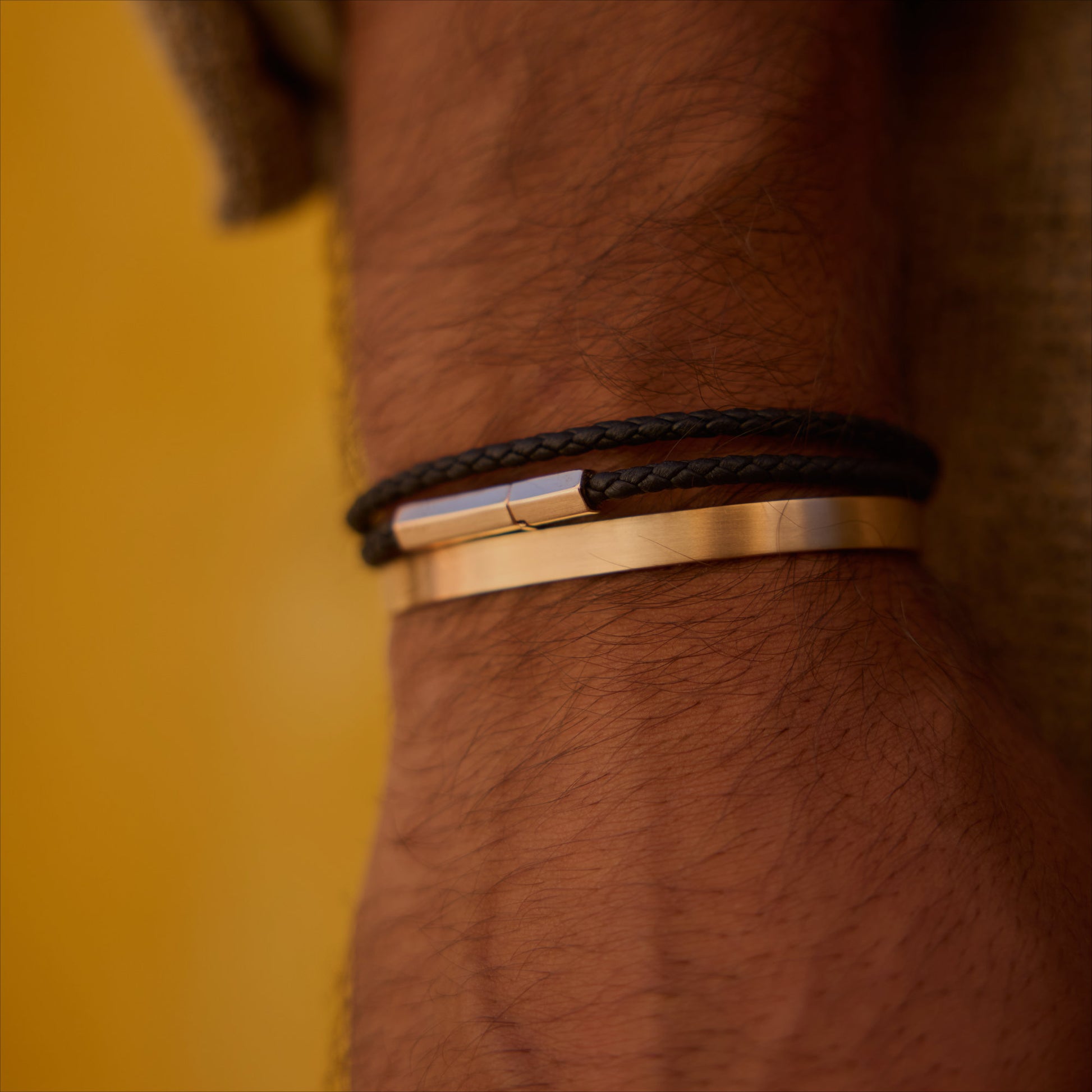 Black double-wrap hexagonal leather bracelet with 18k rose-gold clasp on wrist.
