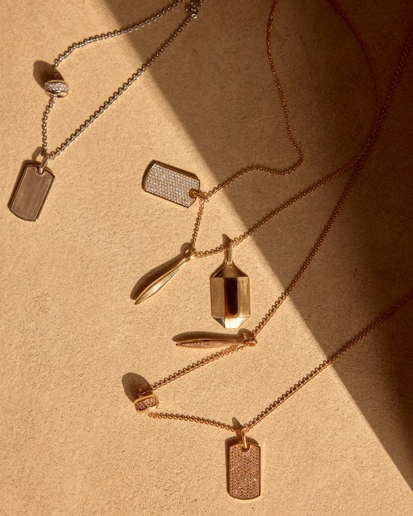 Sculpted gold pendants laid out with their chains: satin-brushed faces flanking a mirror-polished band, the brush direction showing as fine parallel lines and each finish stopping dead at the edge.